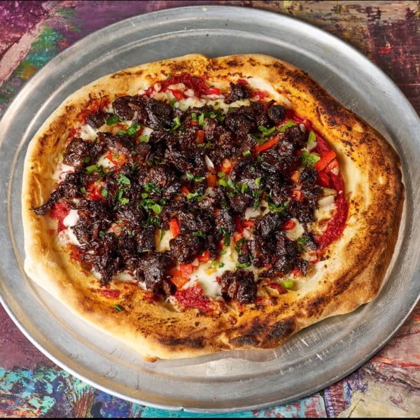 Jamaican jerk chicken pizza with red peppers and cilantro on a metal tray.