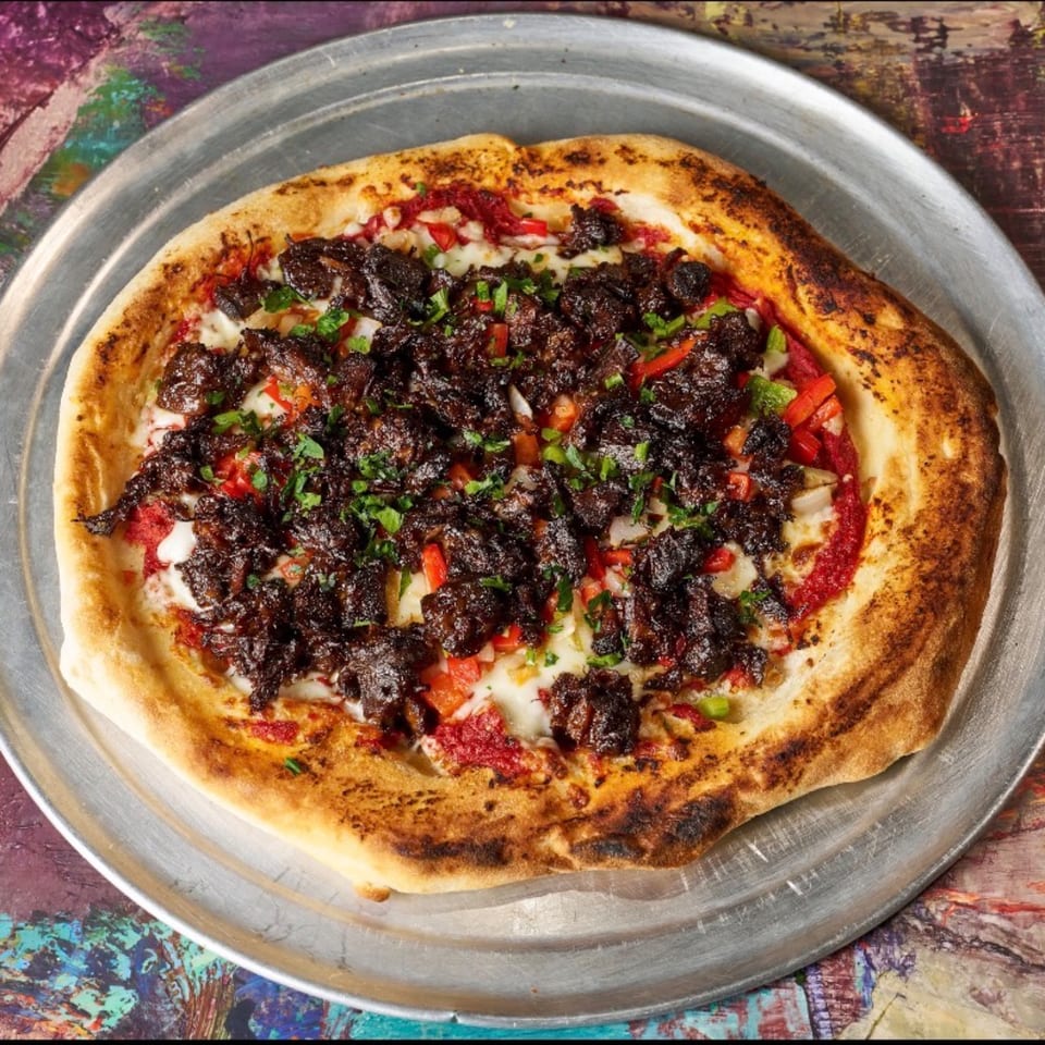 Jamaican jerk chicken pizza with red peppers and cilantro on a metal tray.