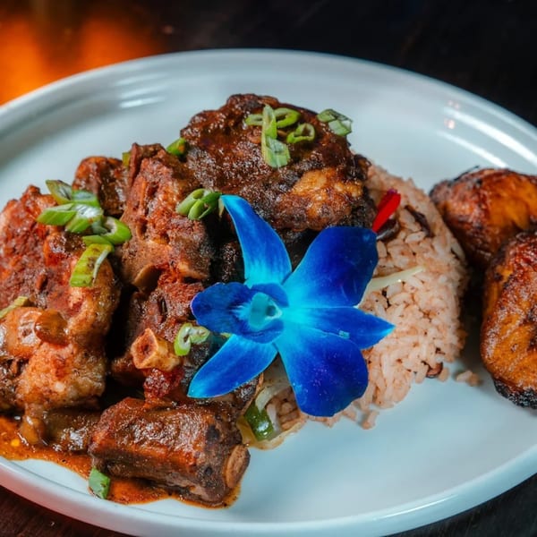 Jamaican oxtail stew with rice and peas, garnished with a blue orchid and scallions.