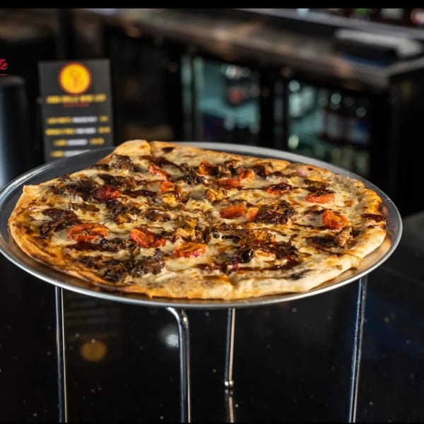 Jamaican jerk chicken pizza with tomatoes and a dark sauce on a metal tray.