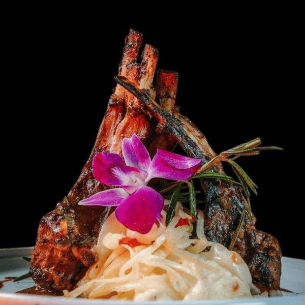 Jamaican jerk lamb chops with coleslaw, garnished with a purple orchid and rosemary sprig.