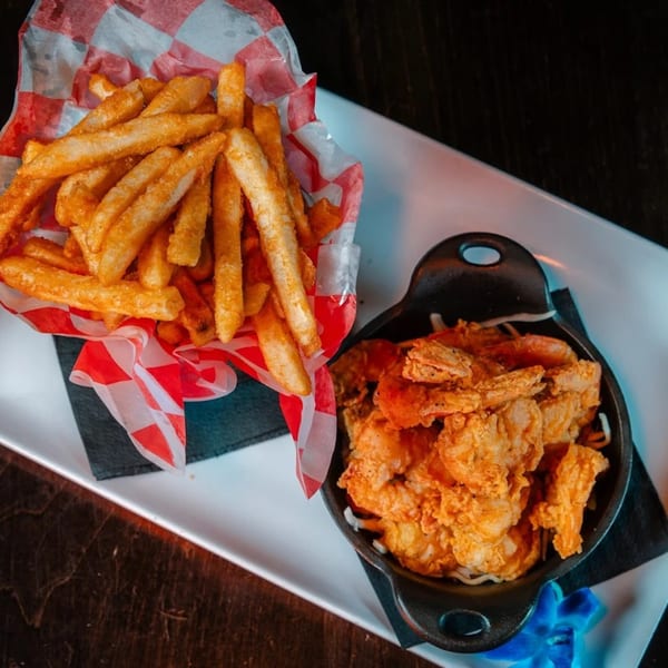 Crispy golden fries in a red and white checkered basket next to a skillet of fried shrimp.