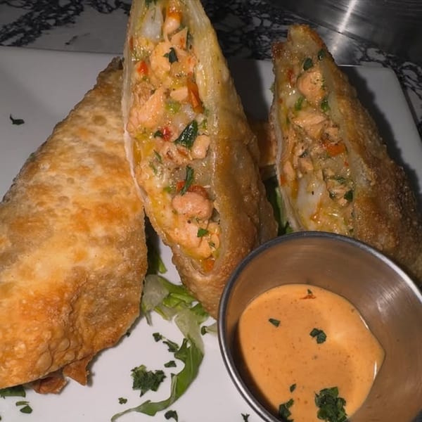 Three golden-brown Jamaican egg rolls, two cut open to show a savory filling, with a side of dipping sauce.