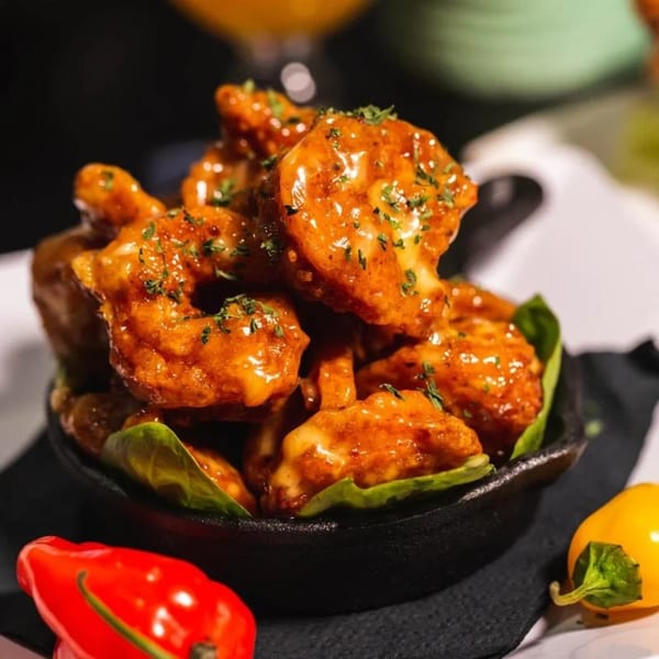 Jamaican jerk shrimp in a black bowl with green leaves, garnished with parsley and peppers.