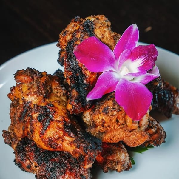 Jamaican jerk chicken pieces, charred and golden brown, garnished with a vibrant pink orchid.