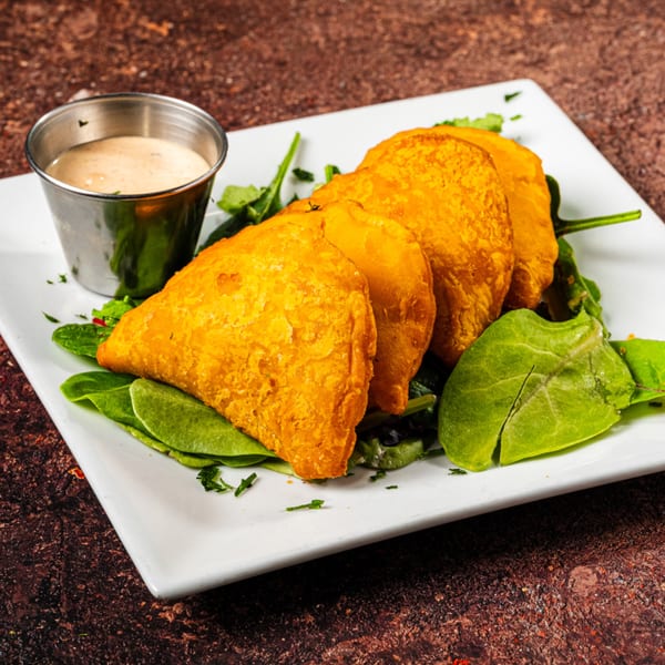 Golden Jamaican patties on a bed of spinach with a side of dipping sauce.