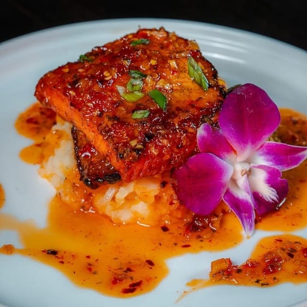 Jamaican jerk salmon with rice, orange sauce, and a purple orchid on a white plate.