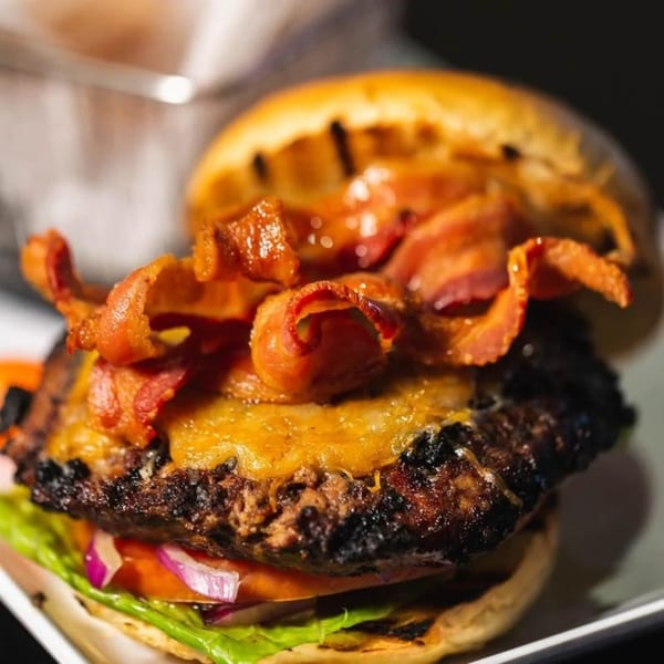 Close-up of a JamaGrille burger with melted cheese, crispy bacon, lettuce, tomato, and red onion.