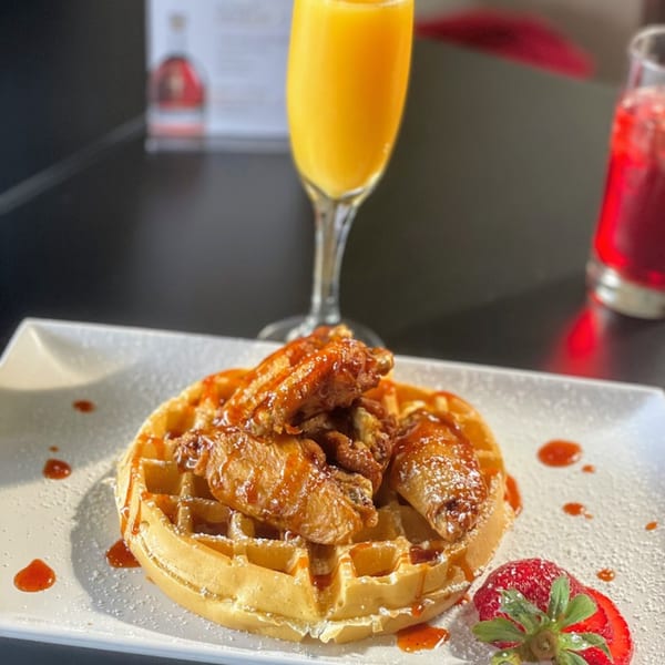 Jamaican fried chicken wings on a waffle with syrup, powdered sugar, and a strawberry.